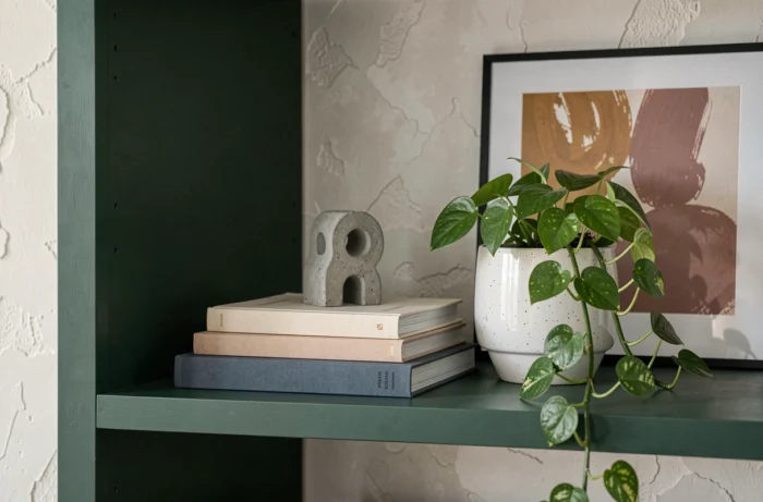 Étagère décorative tendance avec livres d'art, plante verte, objet en béton et cadre abstrait aux tons ocre et rose